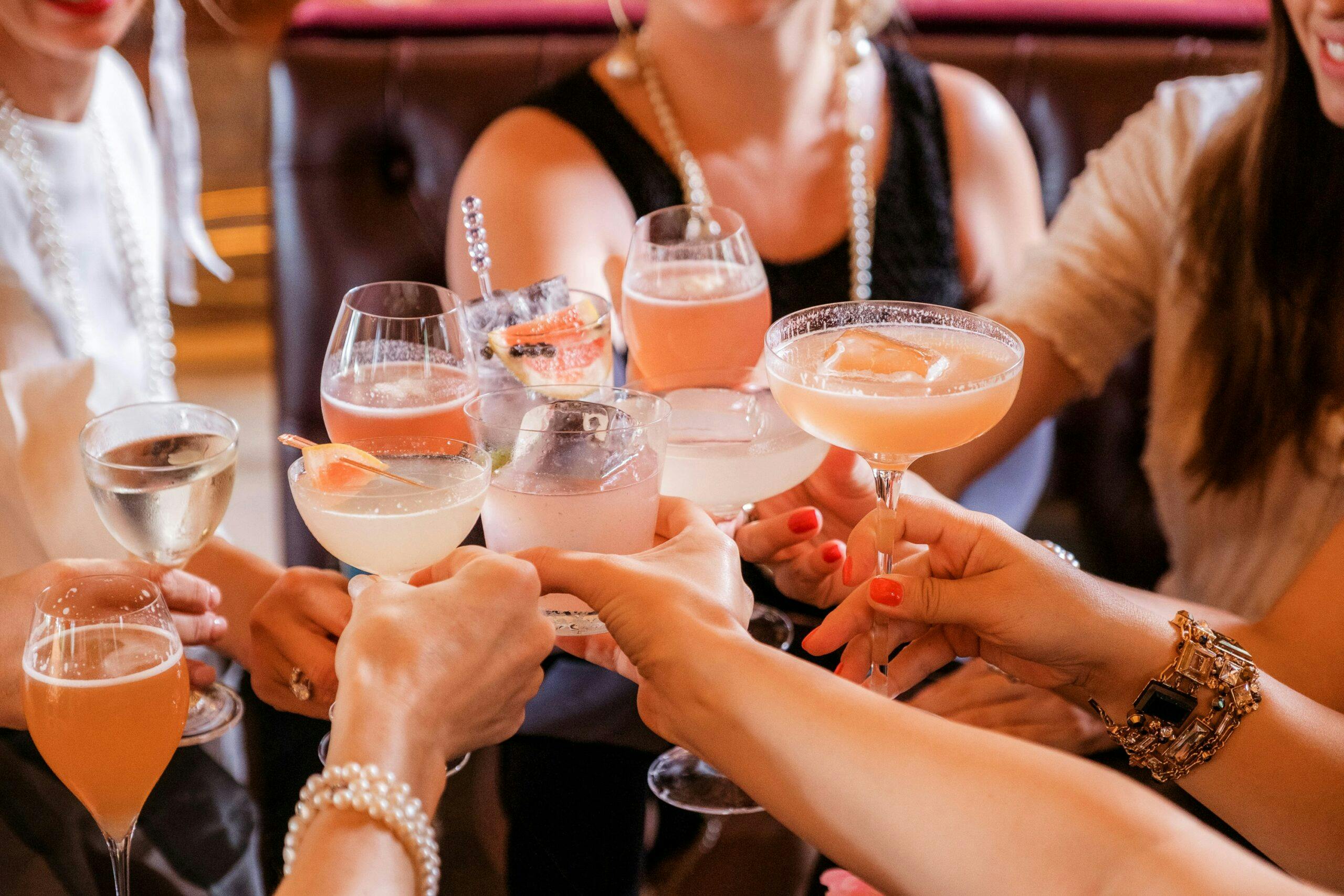 An image of a group of women clinking together various drinks.