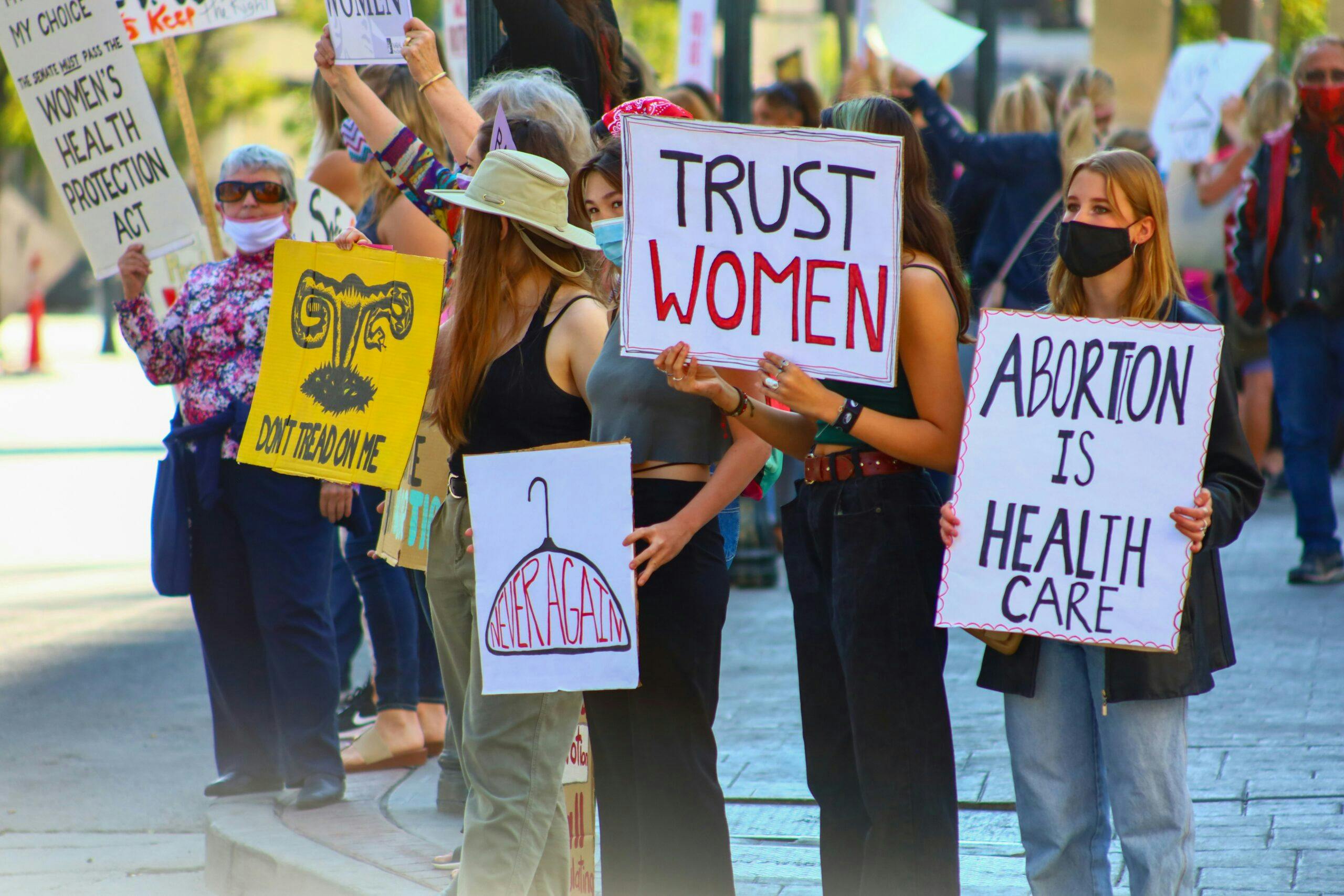 People at a protest, holding up signs with slogans on them like "Trust women", "Abortion is health care" and "Never again".