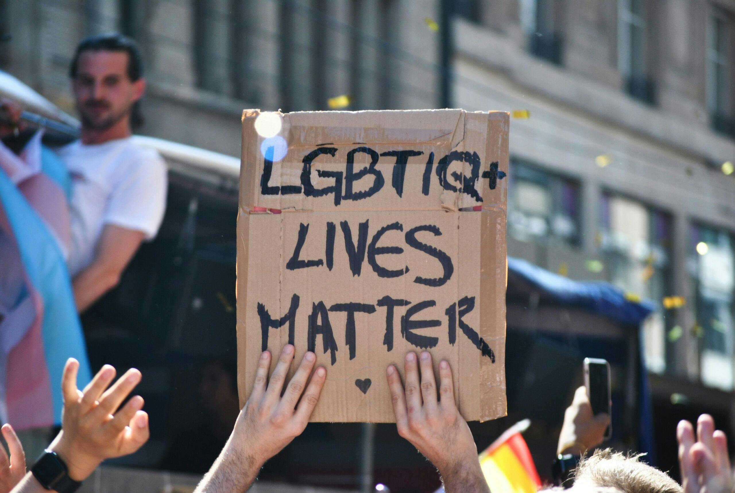A cardboard sign raised in the air at a Pride march that reads "LGBTIQ+ Lives Matter"