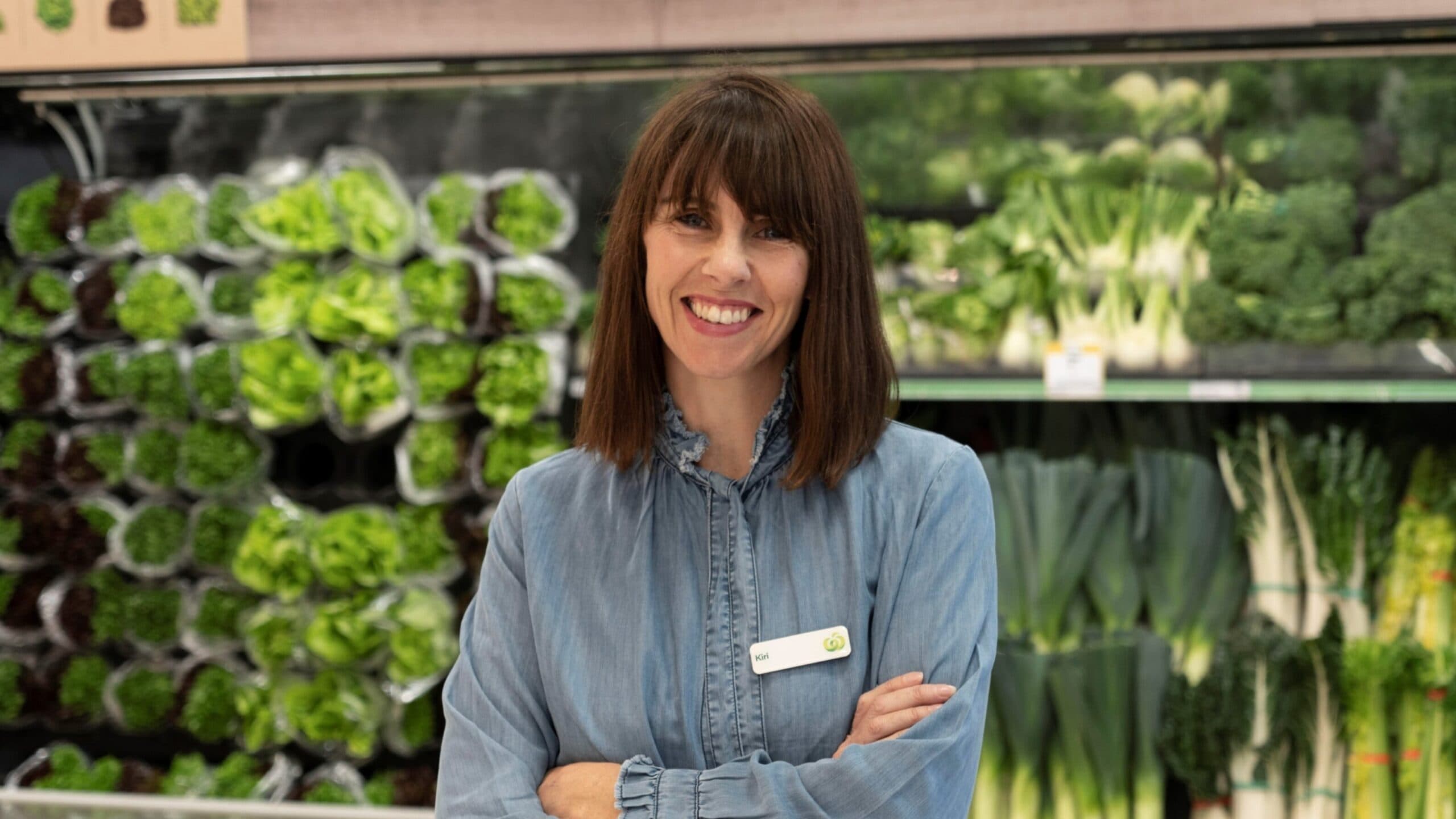 Kiri Hannifin in front of fresh veggies at Woolworths. She wears a name badge.