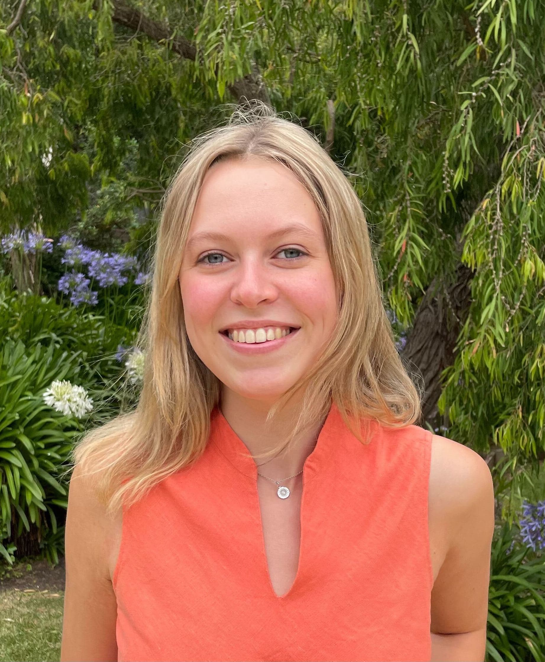 A headshot of Lucie Clairs. She is wearing a bright orange top.