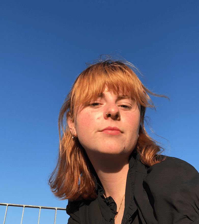 A headshot of Juliette Salom. She wears a black shirt and is pictured against a blue sky.
