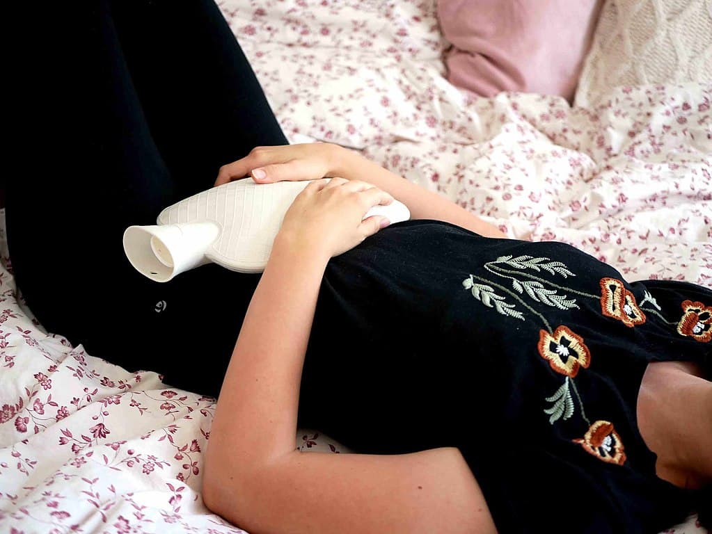 A person lying on a bed while holding a hot water bottle on their tummy.